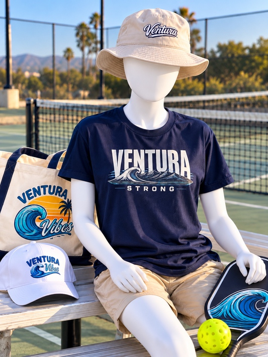 Mannequin with both arms on a pickleball court bench wearing a navy Ventura Strong tee and Ventura bucket hat, with Ventura Vibes accessories and a wave pickleball paddle