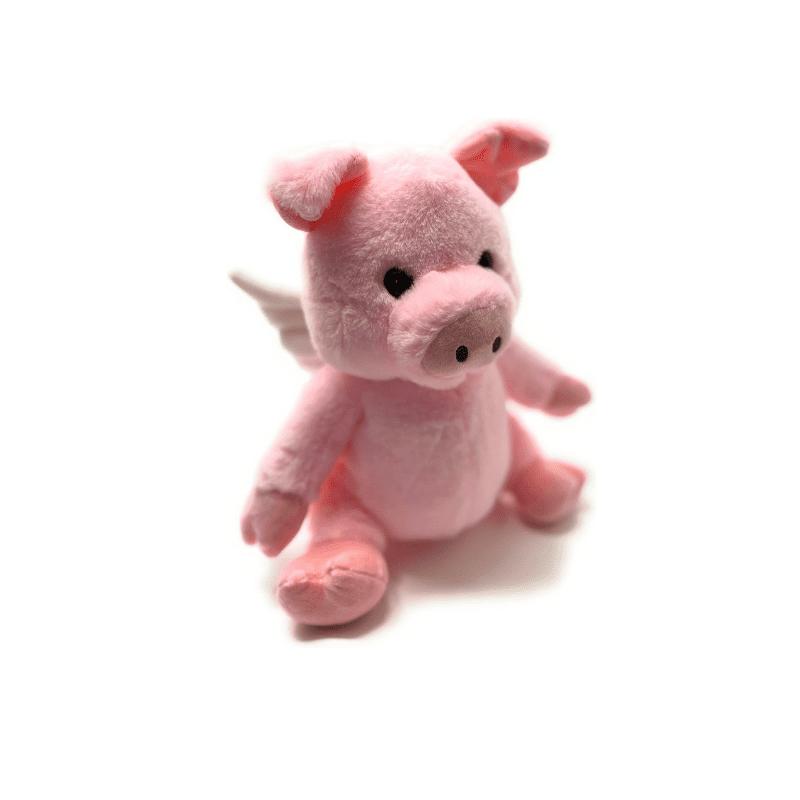 A pink stuffed pig with wings sitting on top of the ground.